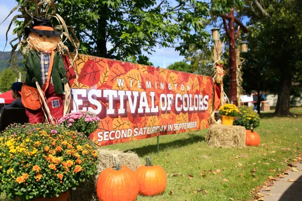 Large Festival of Colors event banner bookended by scarecrows, hay bales, mums, and pumpkins outdoors at park