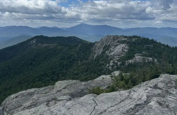 Mountaintop view of a vast, forested landscape under a partly cloudy sky.  Distant mountains are visible on the horizon.