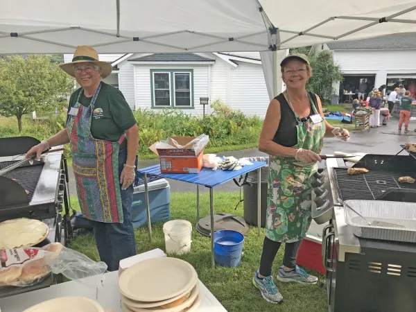 Two senior women cook on grills under pop-up tent at event