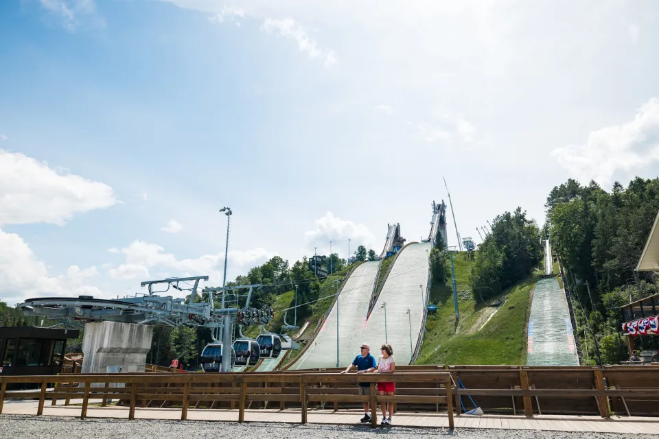 Two Olympic ski jumps stand above the treeline in summer. 