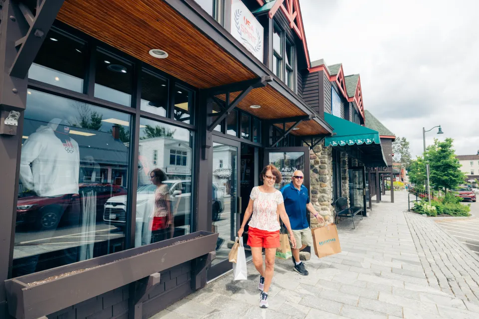 A man and woman walk out of a store on a main street. 