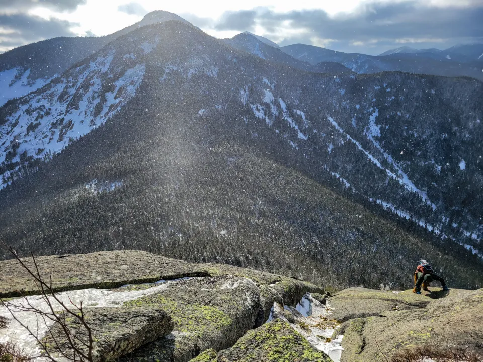 A hiker making his way up a rock slab in the winter mountains.