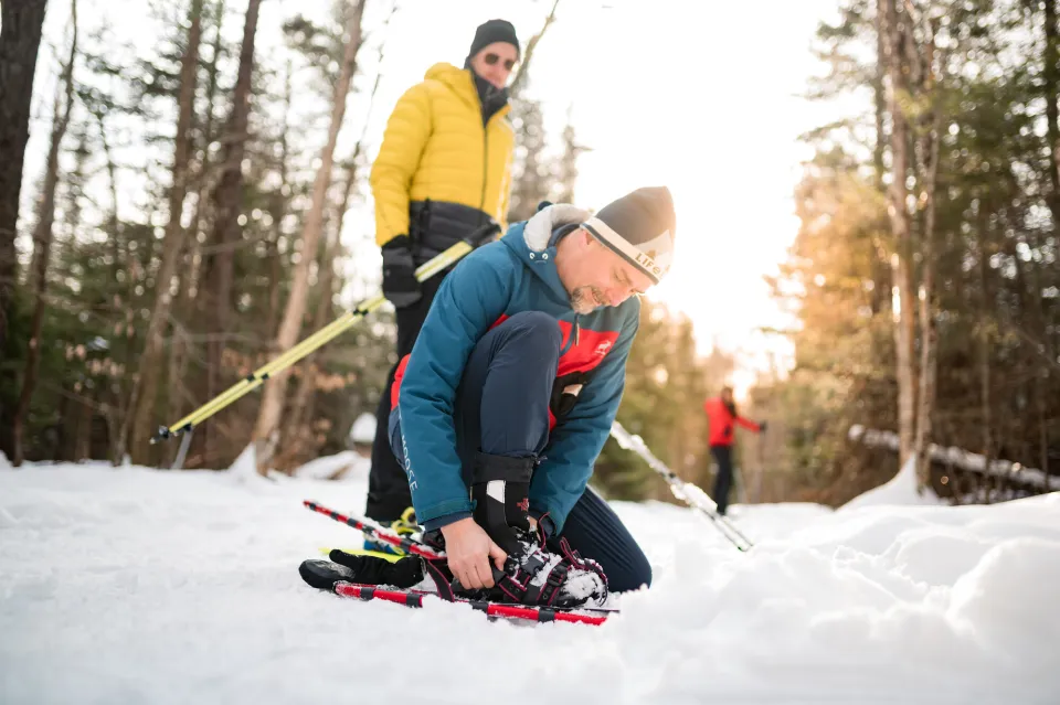 A group of snowshoers putting on their snowshoes in a snowy forest.