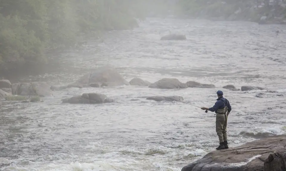 A flyfisher on a rock casting into the morning mist.