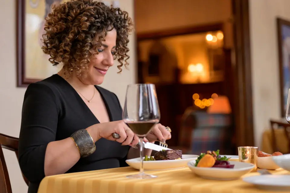 A woman enjoys a glass of wine with dinner at a restaurant.