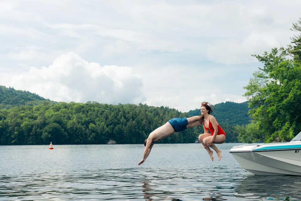 A man and woman jump off a boat into a lake.