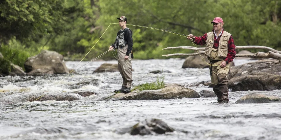 Two men fly fish in a rocky river. 
