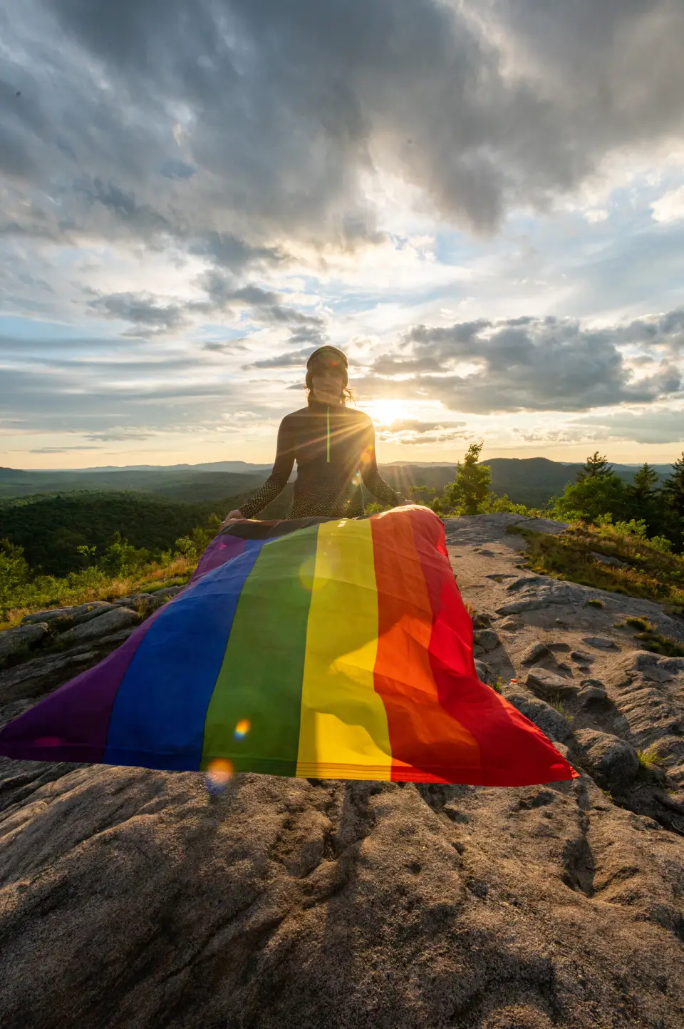 a person stands on top of a mountain with a pride flag