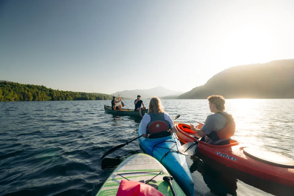 Adults in kayaks cluster together on a lake in the late afternoon sun on a summer day.