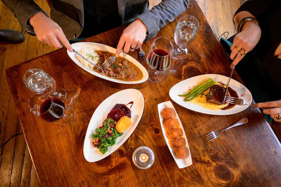 Multiple plates on table with hands holding silverware 