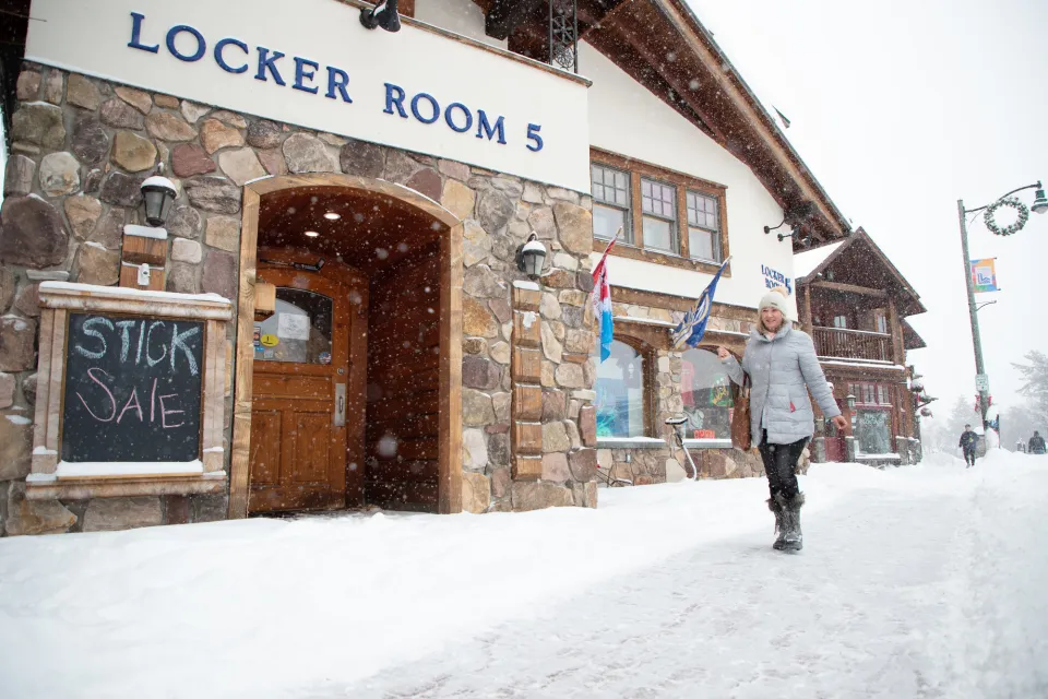 A woman walks on a snowy sidewalk, in front of a business with the name "Locker Room 5" on the front. 