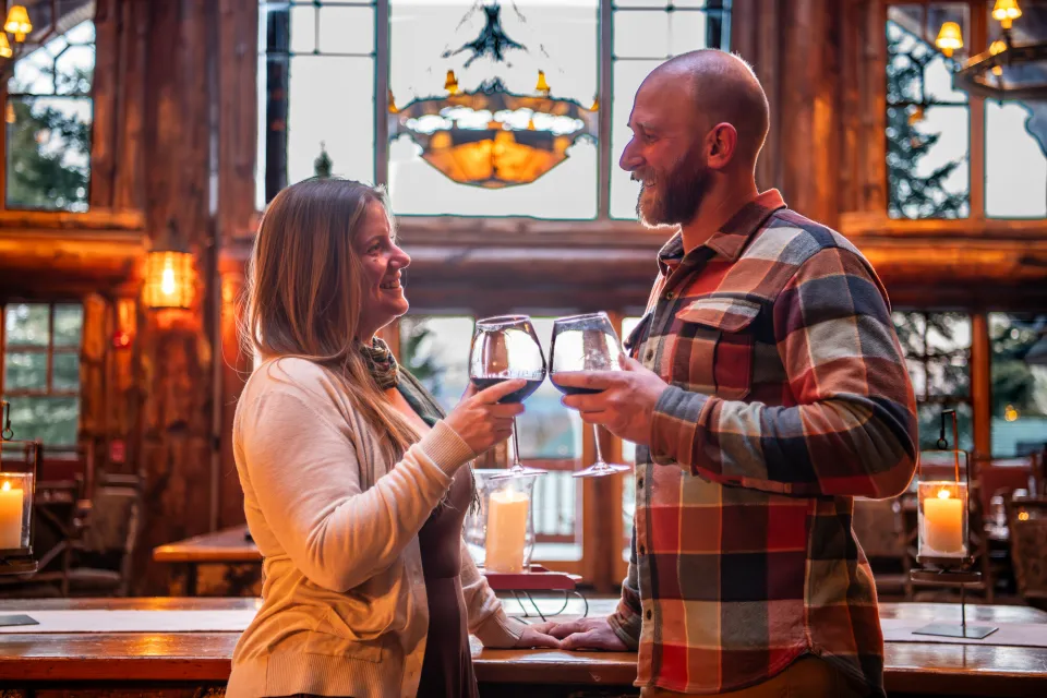 Couple stands in center of large lodge room clinking glasses of red wine