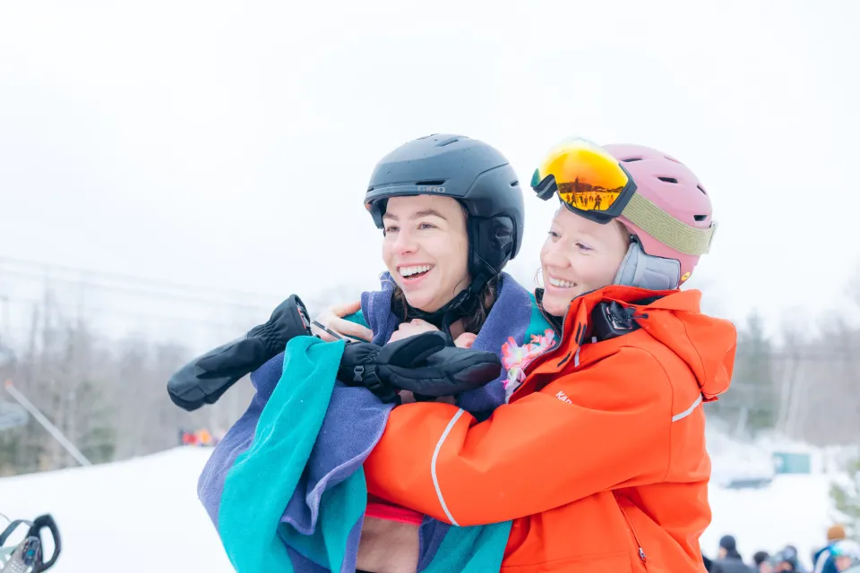 Two women in ski gear laugh and hug. 