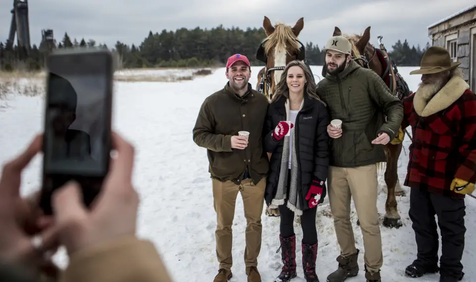 A group of people get their picture taken in front of a horse drawn sleigh