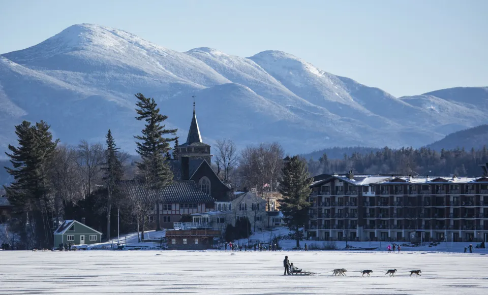 An aerial shot of mirror lake with dog sledding and winter mountains.
