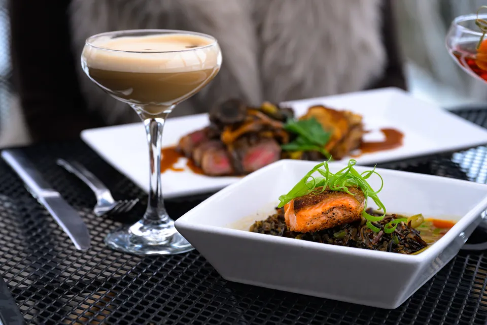 An espresso martini and a plate of salmon and rice on a table. 