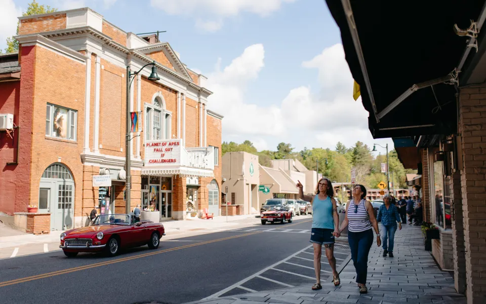 A charming, retro downtown in a small town. People on the sidewalk point into the distance.