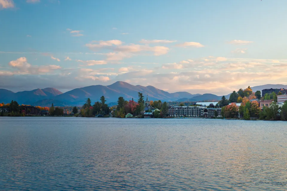 A lake hugged by a small town and mountains in fall.