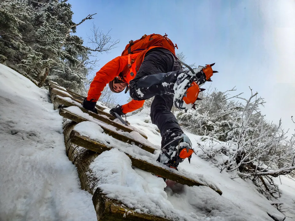 A hiker in crampons going down a ladder in the winter.