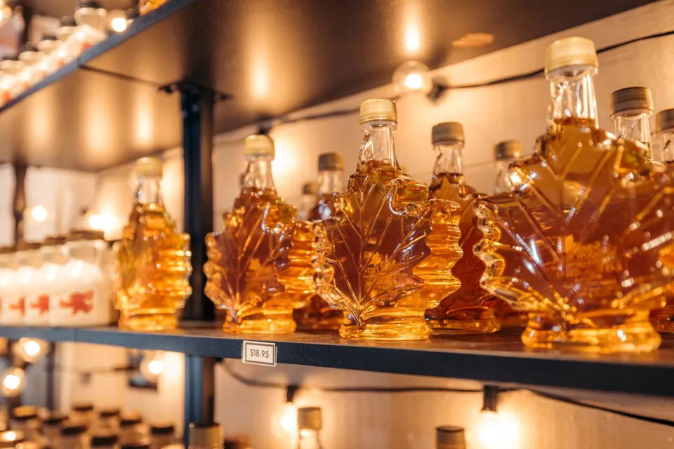 Glass maple leaf jars on shelf filled with golden maple syrup