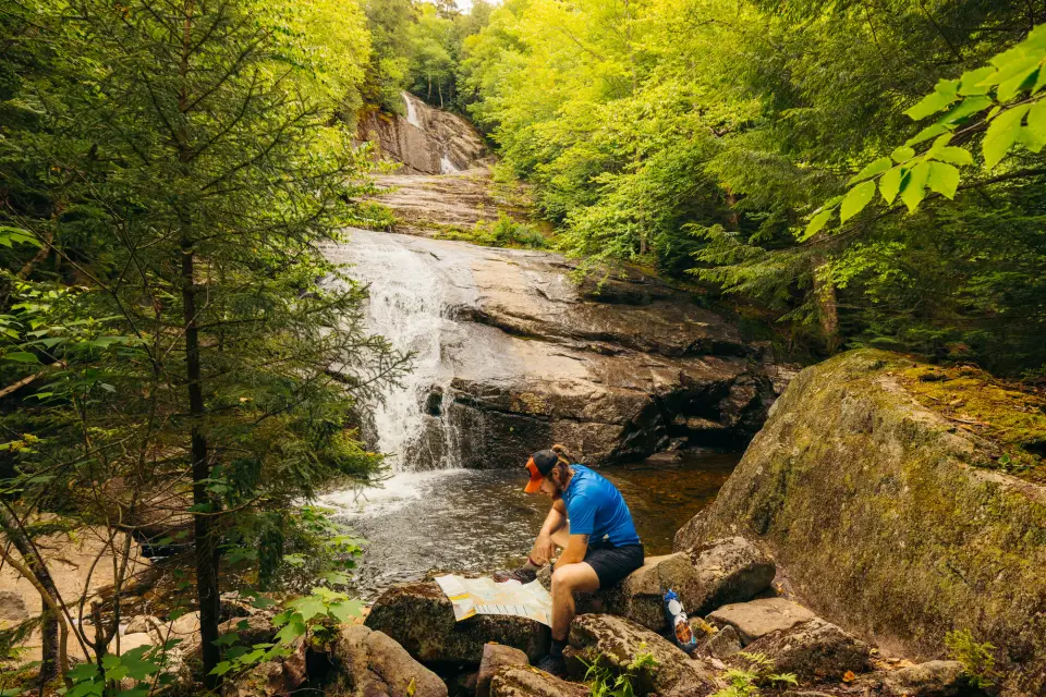 A man reads a map next to a waterfall.