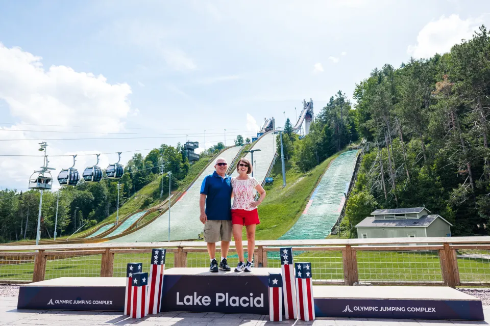 A man and woman stand on an awards podium in front of ski jumps in summer. 