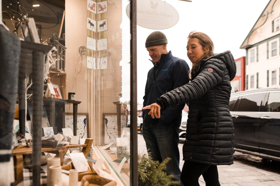 A man and woman in winter jackets window shop at a jewelry store.