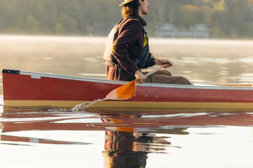 A man canoes on a lake in the early morning.