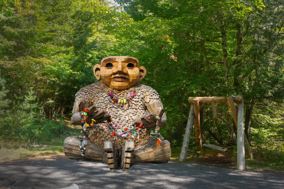 A wooden troll sits at the edge of a parking lot.