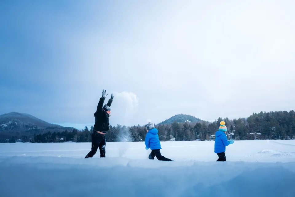 Father throws snow in the air over two small children next to frozen lake with mountains in background