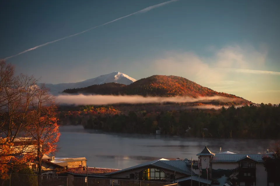 A fall mountain range looks over a lake and town in autumn.