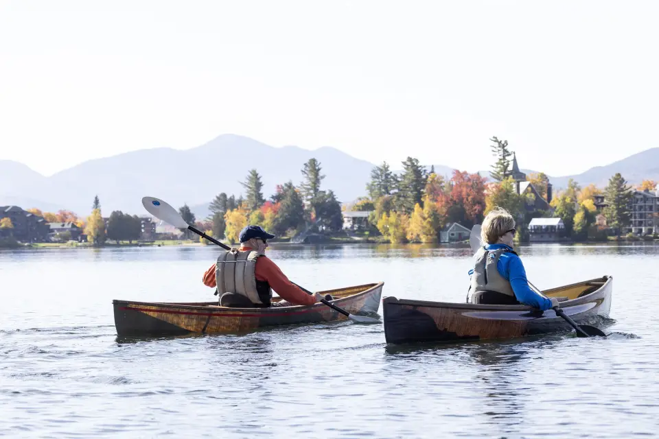 Two people paddling solo canoes on a lake.