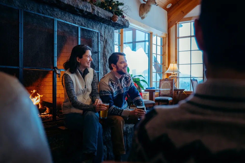 Couple sits on heart of stone fireplace talking to people nearby