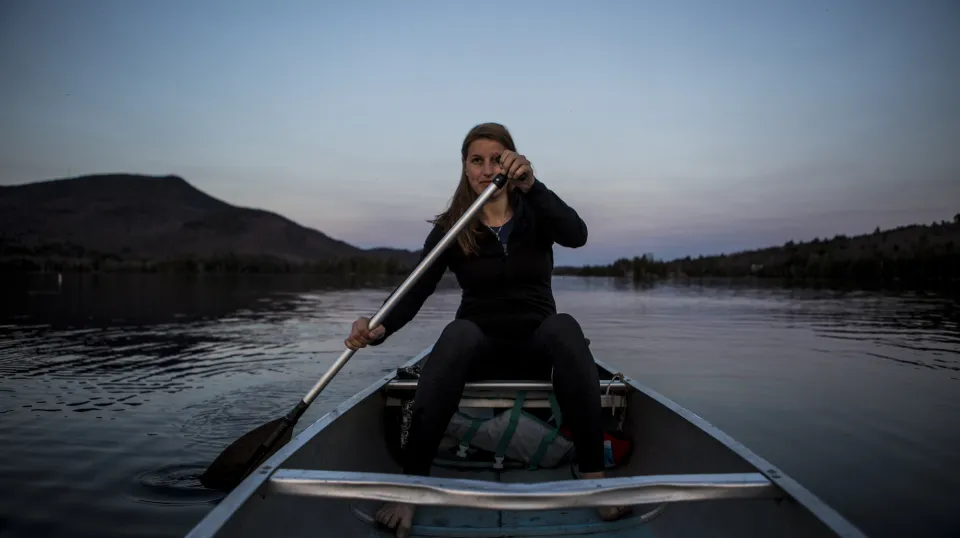 A woman paddling a canoe a dusk.