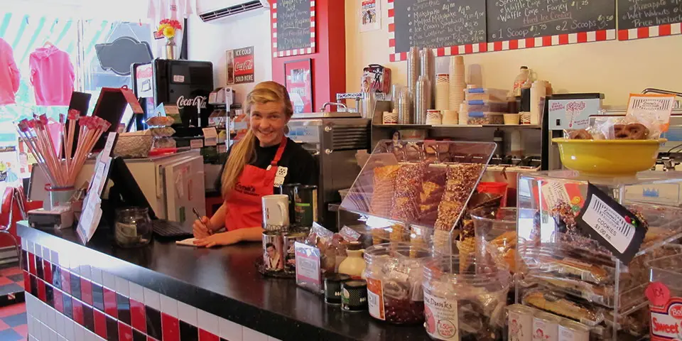 A young woman poses behind an ice cream counter.