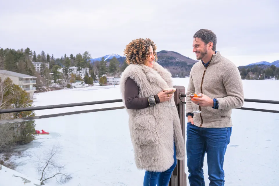 Couple stands on upper porch over frozen Mirror Lake with cocktails