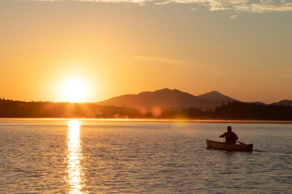 A person canoeing on calm water during sunset.