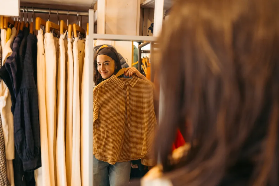 A woman looks at a jacket in the mirror. 