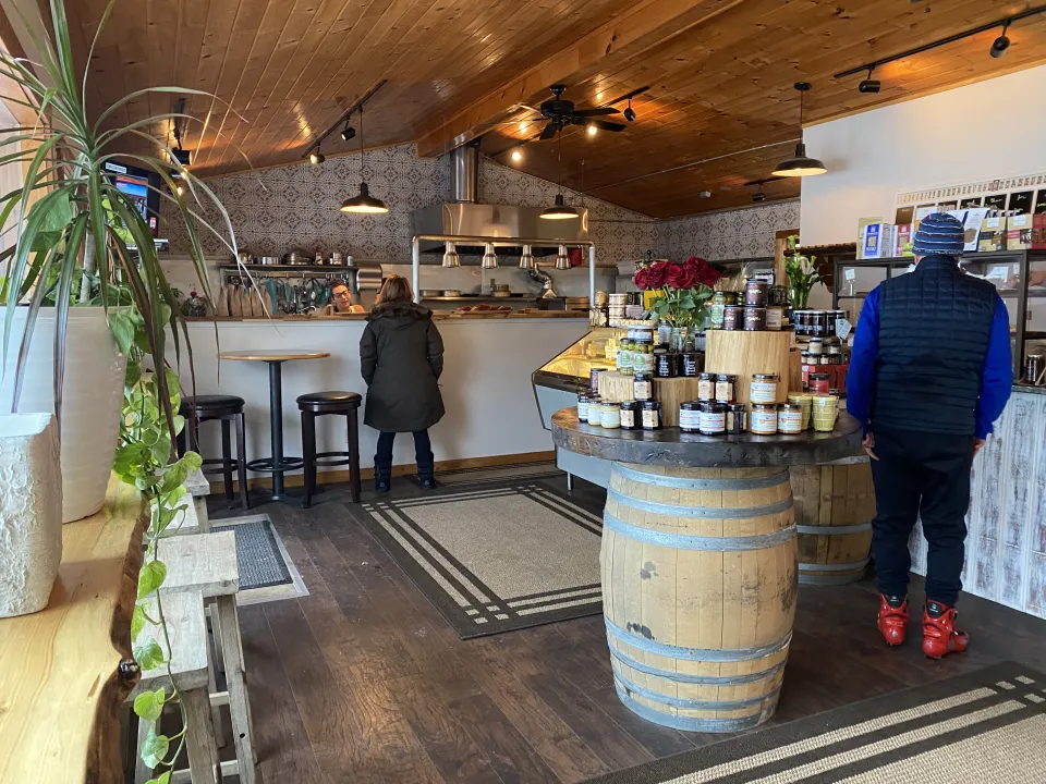 People line up inside a cozy bakery for pastries and cheese.