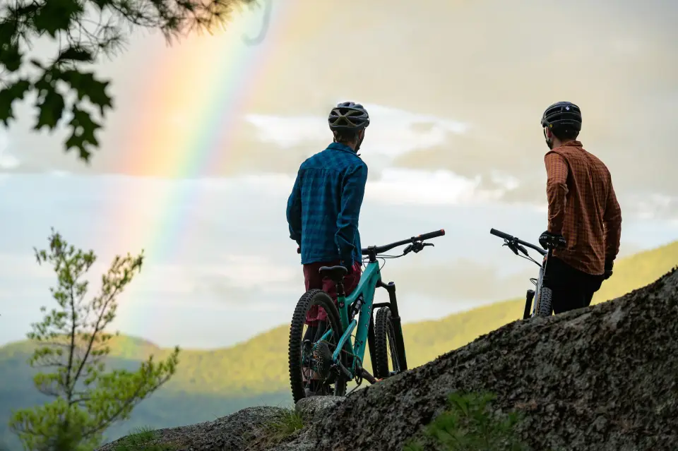 Two men sit on their bikes on a mountain side.