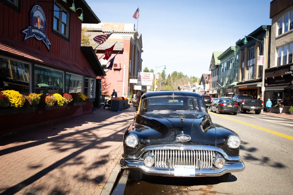 A classic car is parked along a sidewalk on a sunny day in a small town.