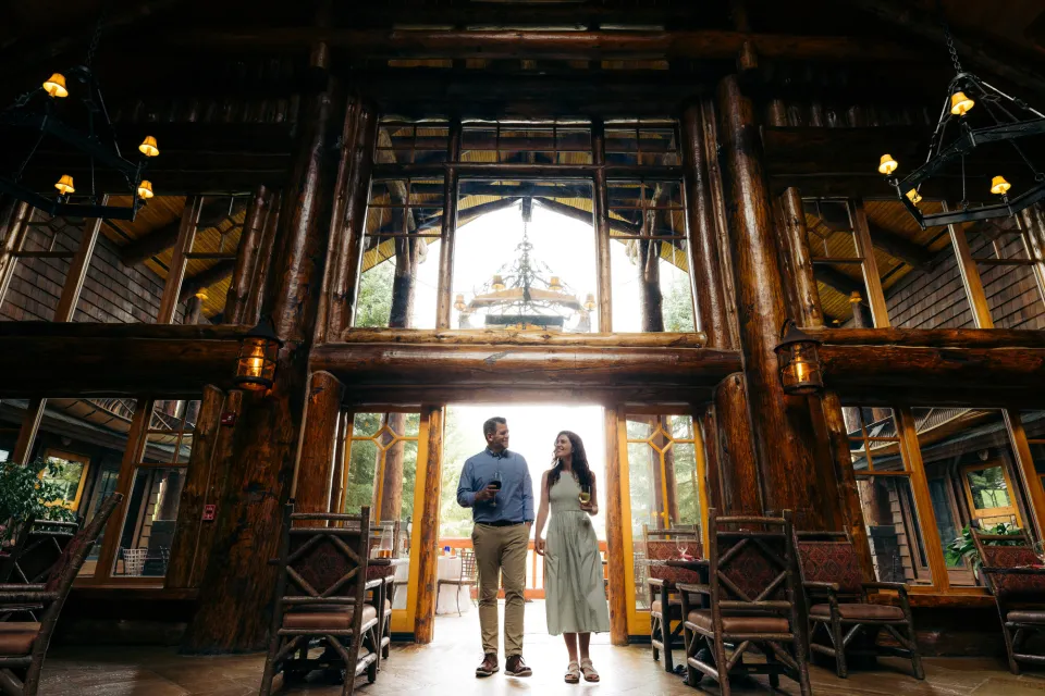 A man and woman walk through a grand entrance of a lodge. 