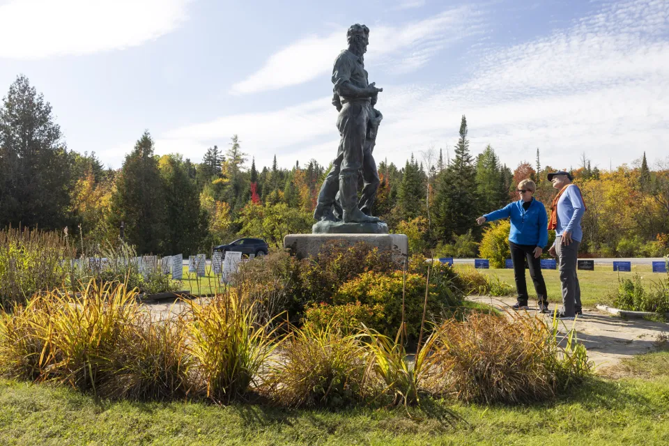 A man and woman look at a statue in a fall field. 