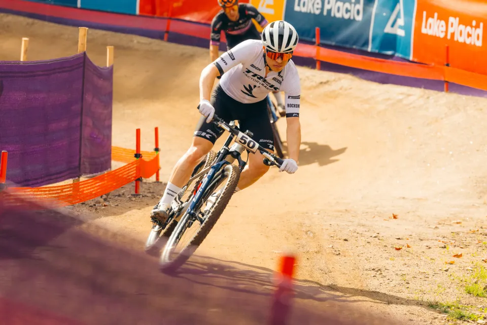 Mountain bike competitor in full gear rides bike on dirt track with event fencing on either side