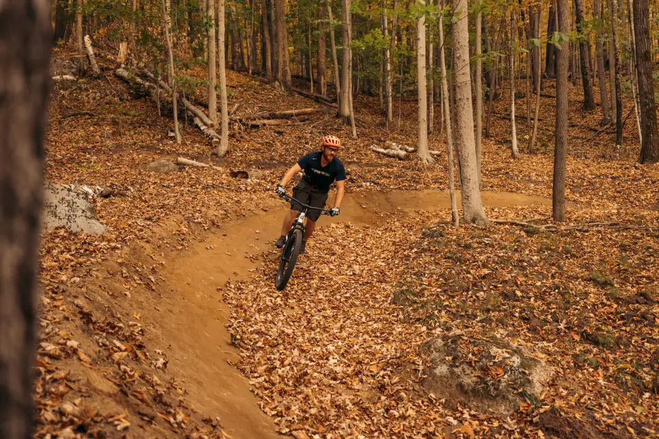 A person mountain biking on a trail with fall foliage.