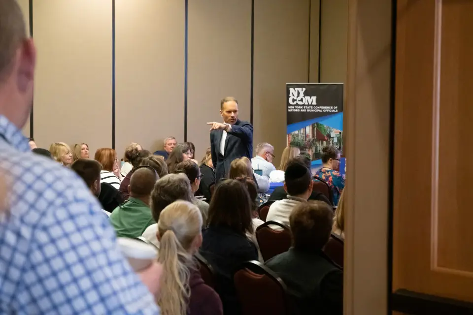 A man in a suit gives a presentation to a room full of people.