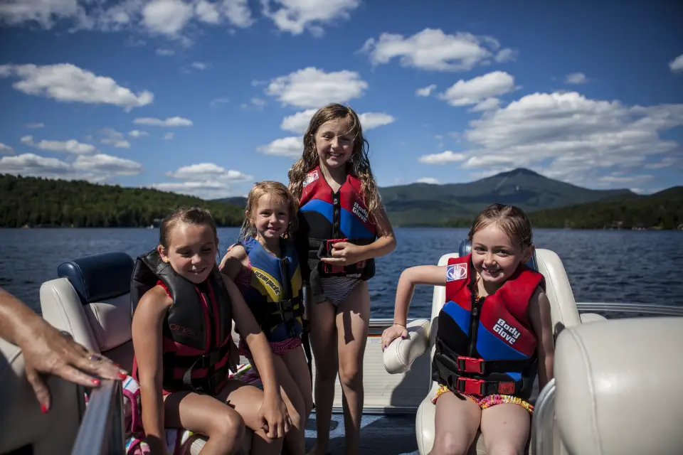 Children wearing PFDs smile on a motorboat under a sunny sky.