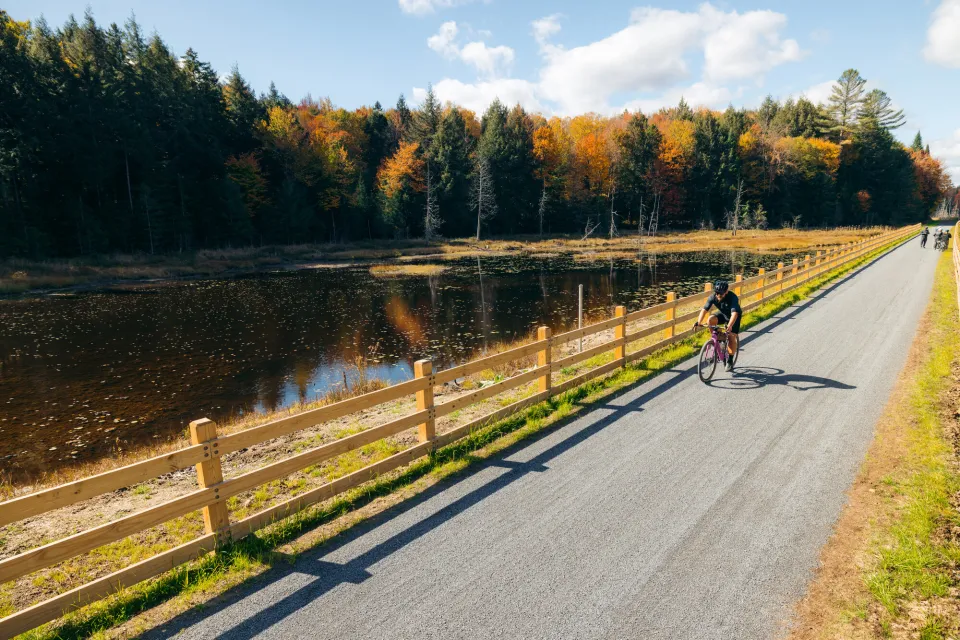 A biker on a gravel bike path by the water in the fall