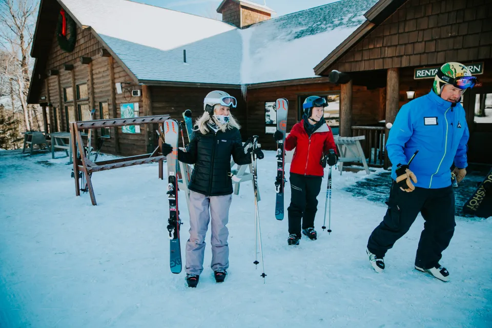 Two women and a man in ski gear walk out of a ski lodge in winter. 