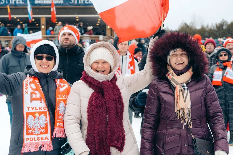 A group of spectators smiling and bundling up during a winter event in Lake Placid.